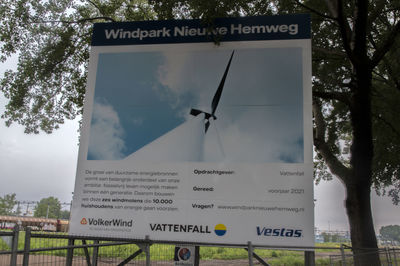 Information sign by trees against sky