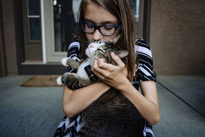 A pre teen girl kissing her cat on the front porch