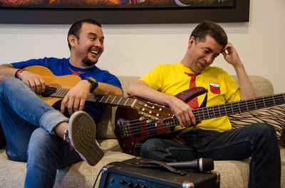 Smiling men with guitars sitting on sofa at home