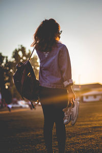 Rear view of woman with umbrella walking on street during sunset