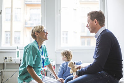 Side view of mature female doctor talking to man while son standing in background at medical clinic