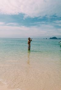 Side view of woman shielding eyes while standing in sea against sky