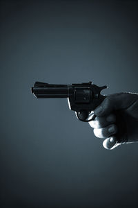 Cropped hand holding gun against clear sky