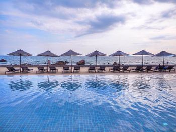 Lounge chairs by swimming pool in sea against sky