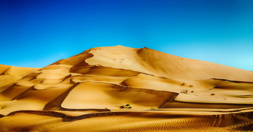 Sand dunes in desert against clear blue sky