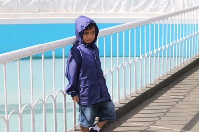 Cute boy wearing raincoat while leaning on railing