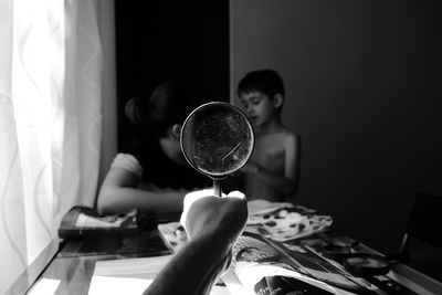 Cropped image of hand holding magnifying glass against mother and son at home