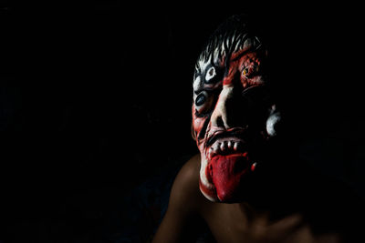 Close-up of man wearing spooky mask against black background