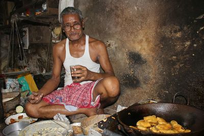 Senior man holding glass by cooking utensil at shop