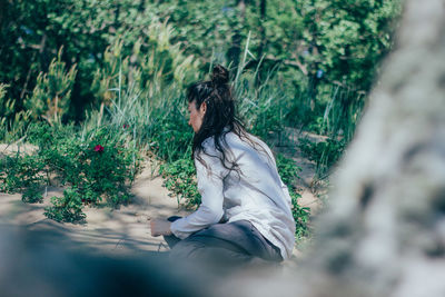 Woman sitting on sand against trees