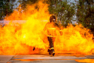 Full length of firefighter walking in fire on road against trees