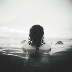 Rear view of woman in infinity pool by sea against clear sky