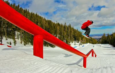 Man skateboarding over railing at snow covered field