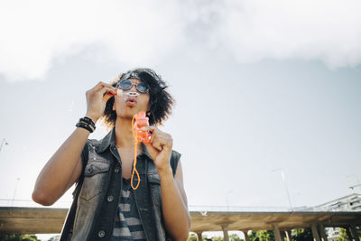 Low angle view of young man blowing soap bubbles against sky