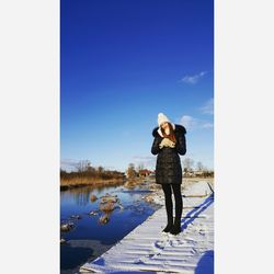 Rear view of woman standing by lake against sky