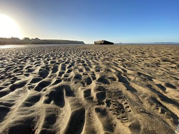 Footprints on sand at beach against clear sky