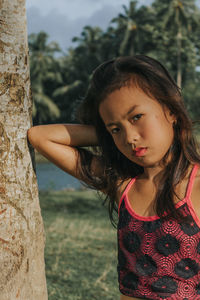 Portrait of young woman standing against tree