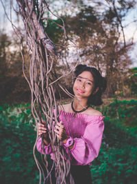 Portrait of woman standing by tree in forest