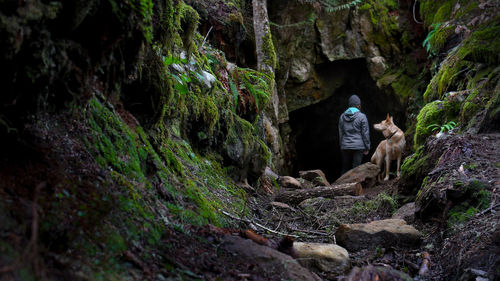 Woman with dog on rocky pathway against cave at forest