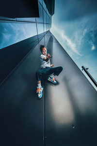 Young man sitting on wall against sky