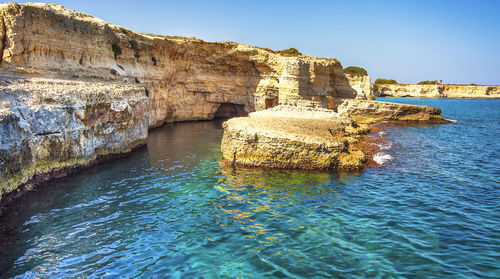 Rock formation by sea against clear blue sky