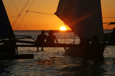 Rear view of couple sitting on outrigger boat in sea against sky during sunset