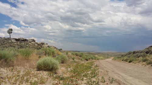 Dirt road amidst landscape against sky