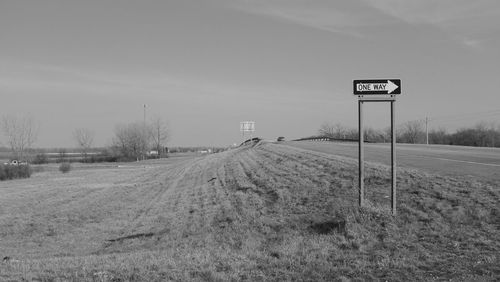 Road sign on field against sky