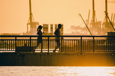 People on pier over river against sky during sunset