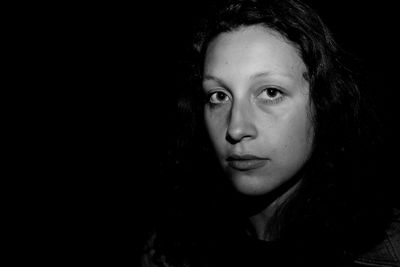 Portrait of serious young woman against black background