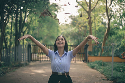 Young woman with arms raised standing by tree