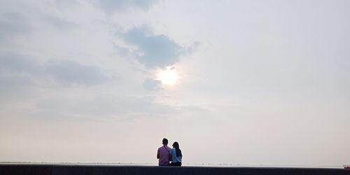 Couple sitting against sky during sunset