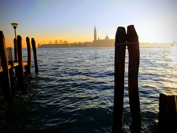 Wooden posts in sea against sky during sunset