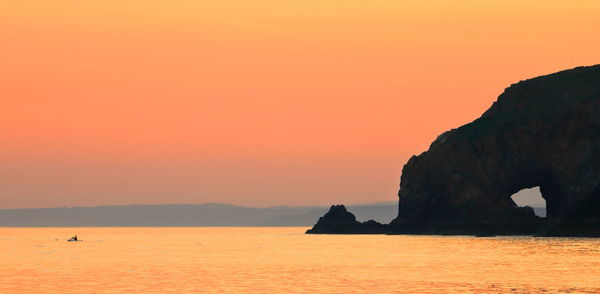 Silhouette rock in sea against sky during sunset