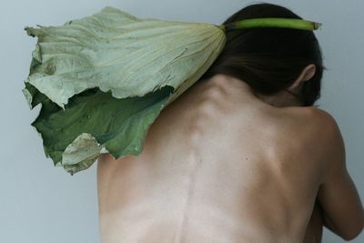 Rear view of shirtless depressed woman with leaf sitting by wall