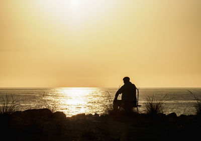 Silhouette man looking at sea against sky during sunset