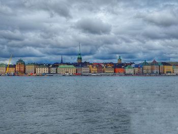 View of buildings by river against cloudy sky