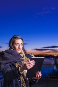 Young woman using digital tablet against sky during sunset