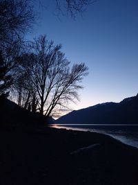 Silhouette bare tree by lake against sky during sunset