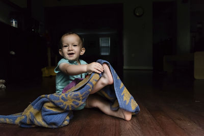 Portrait of cute baby boy playing with towel while sitting on floor at home