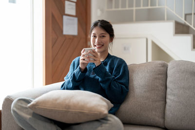 Young woman using phone while sitting on sofa at home