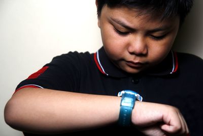 Close-up of overweight boy checking time against wall