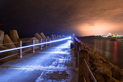 Light trail on footpath amidst sea at night