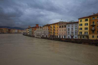 Buildings at waterfront against cloudy sky