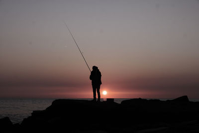 Silhouette man walking on beach against sky during sunset