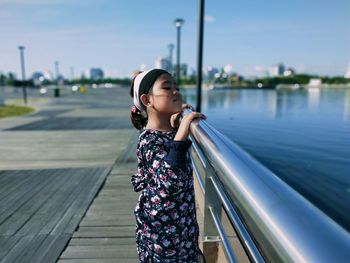 Full length of young woman standing on railing against sky