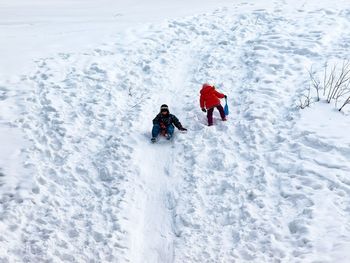 High angle view of siblings playing on snow covered landscape during winter