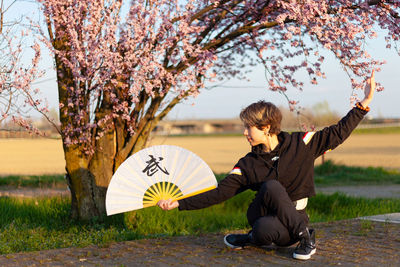 Young caucasian woman posing a wushu martial art posture in a sunny day, a pink tree in background