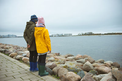 Rear view of brother and sister looking at sea standing against sky