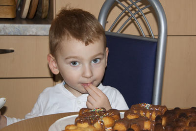 Portrait of cute boy eating cookies on table at home